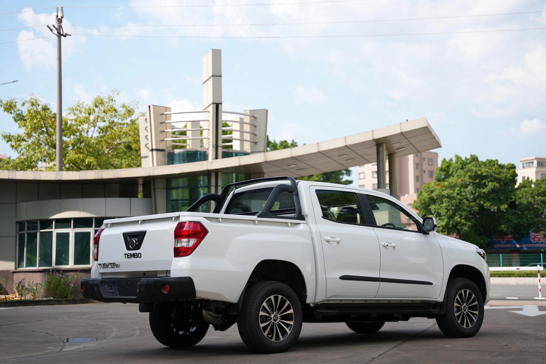 Rear view of a white Tembo Tusker dual-cab electric ute with sports bar parked outside a modern building