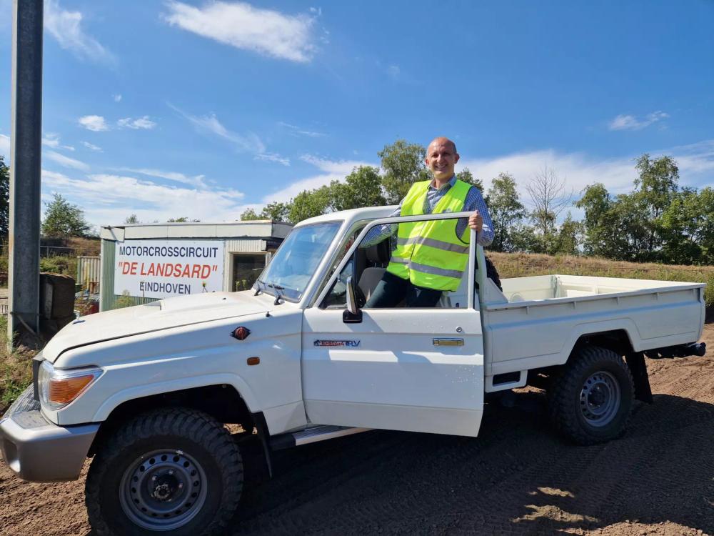 Smiling man in a hi-vis vest in the door of a Tembo 4x4 e-LV single-cab Land Cruiser at De Landsard circuit, Eindhoven