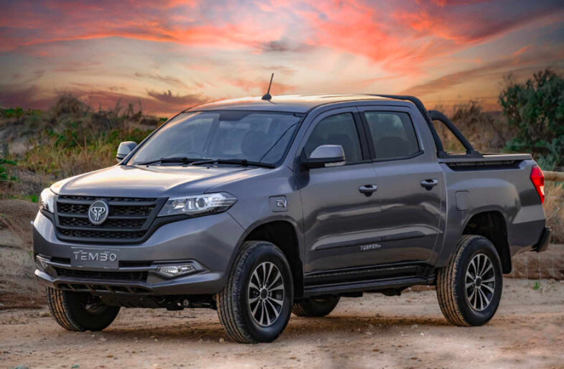 Grey Tembo Tusker dual-cab electric ute parked on a dirt track under a pink sunset sky