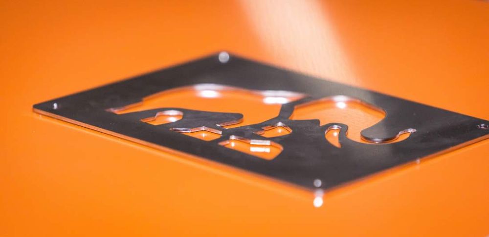 Close-up of a laser-cut steel plate featuring the Tembo elephant logo, resting on an orange surface