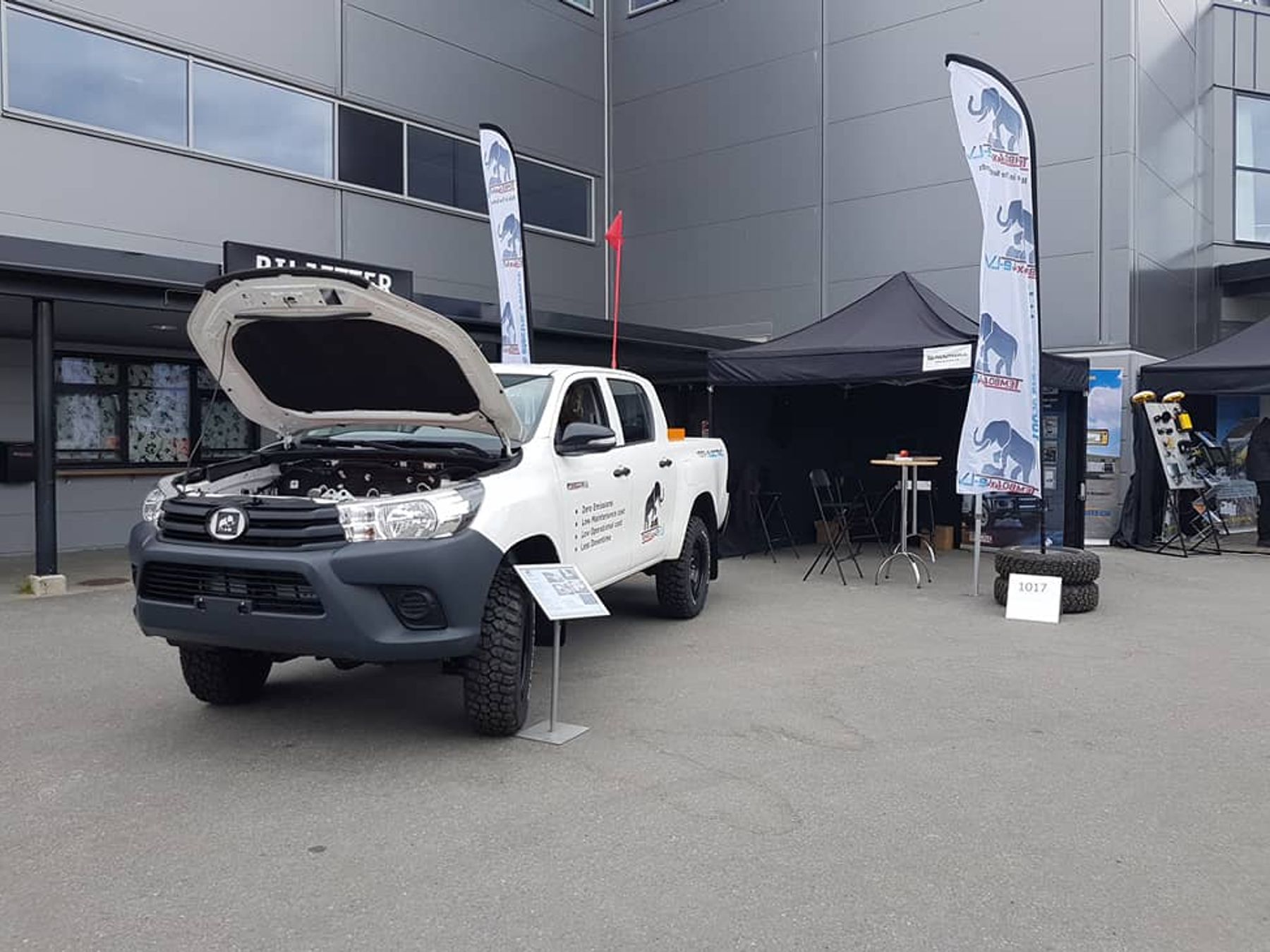 Electric Toyota Hilux dual-cab with bonnet raised at the Tembo 4x4 e-LV stand, with branded flags and a black gazebo