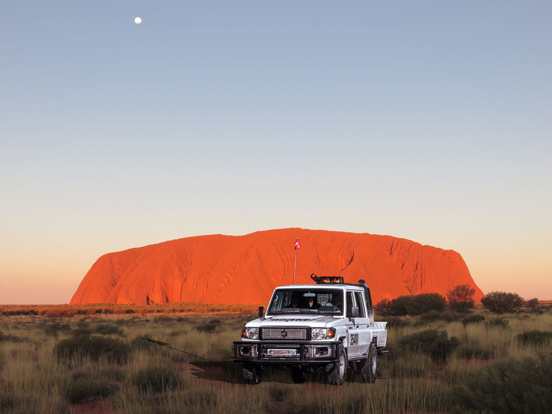 Tembo 4x4 e-LV dual-cab Land Cruiser in outback grassland in front of Uluru at sunset