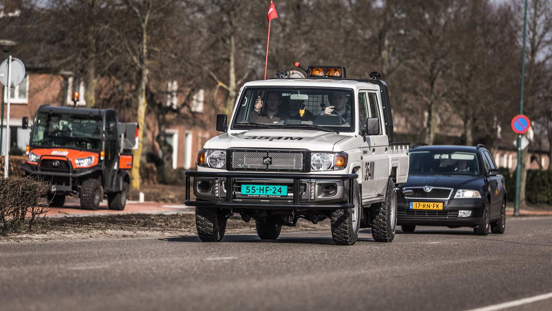 Tembo electric Land Cruiser 70 series dual-cab with roof beacons and safety flag driving on a town street