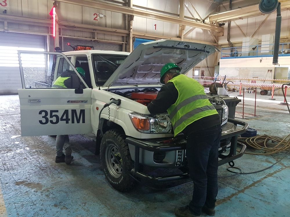 Workers in hi-vis vests and hard hats checking the Boliden Tembo 4x4 e-LV under its open bonnet in a mine workshop