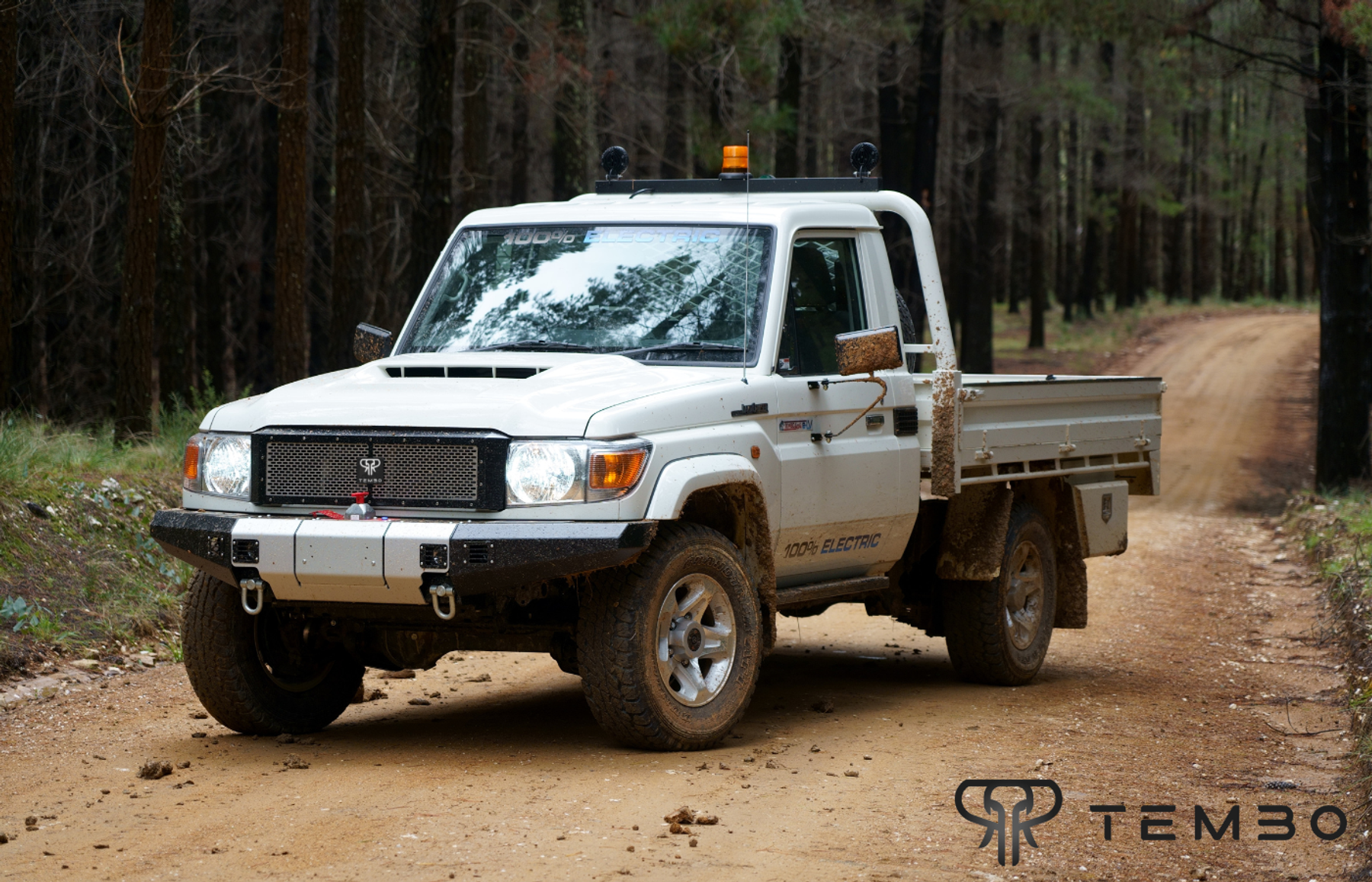White electric Toyota Land Cruiser 70 series single-cab with tray on a muddy forest track, Tembo logo
