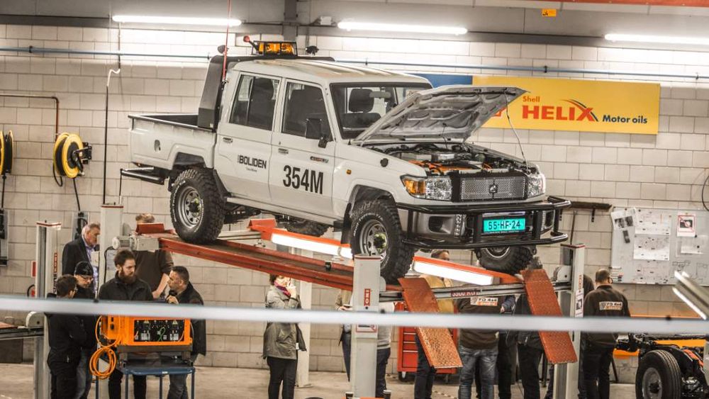 Boliden-branded Tembo 4x4 e-LV Land Cruiser dual-cab on a workshop hoist, bonnet open, as visitors look on