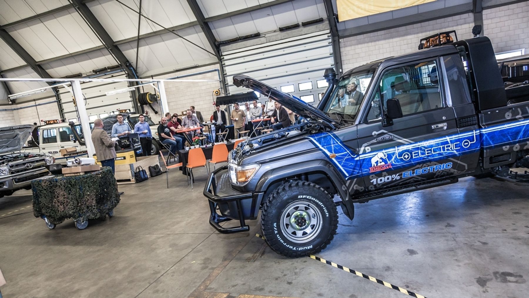 Guests listening to a presentation in the workshop at the Tembo 4x4 e-LV prototype launch, with the Electric Cruiser in front