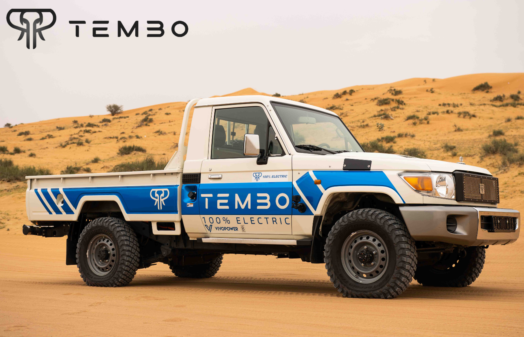 Tembo 100% electric Land Cruiser 70 series single-cab ute in white and blue livery among desert sand dunes