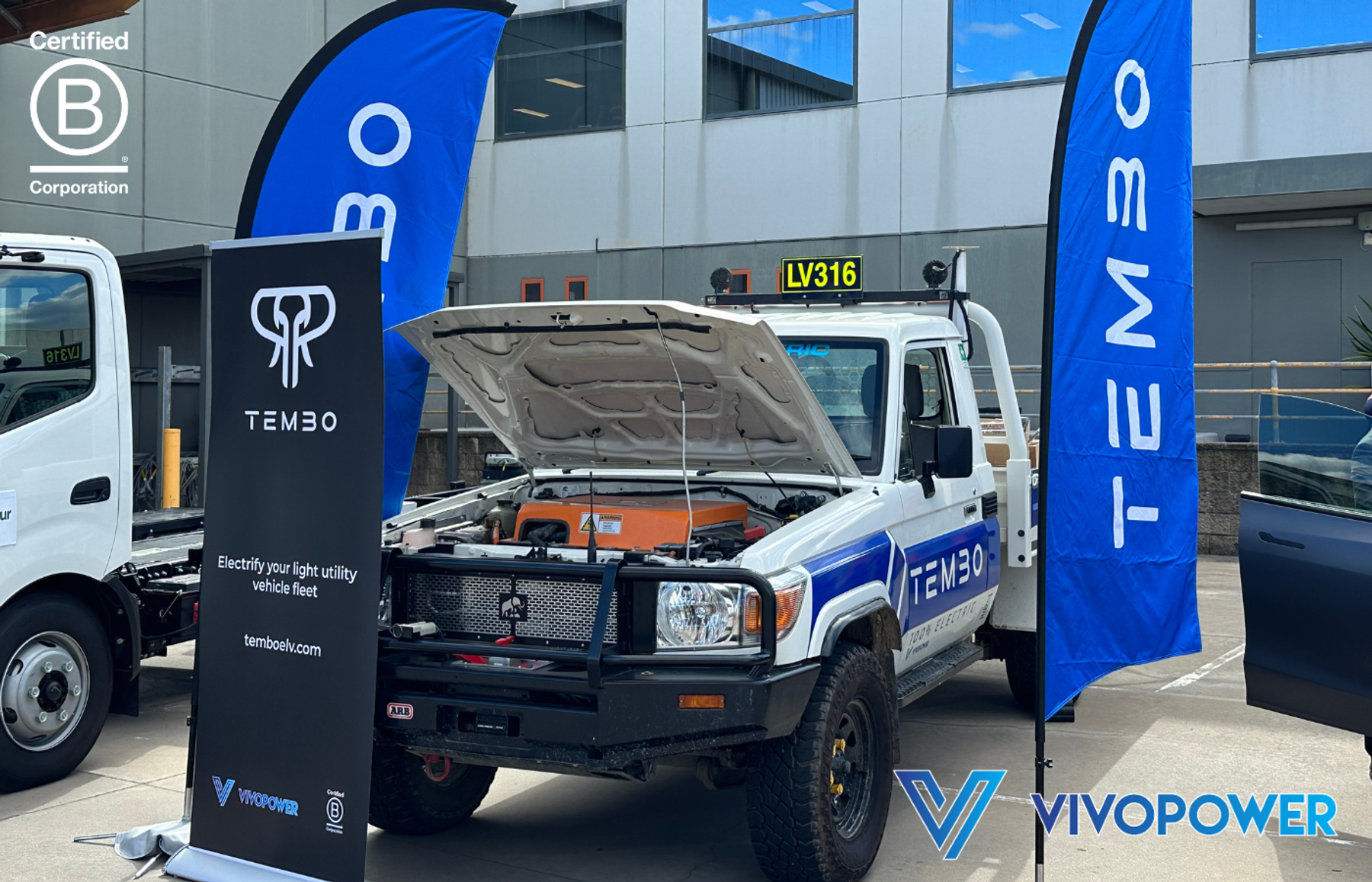 Tembo electric Land Cruiser with bonnet open between Tembo flags and an 'Electrify your light utility vehicle fleet' banner