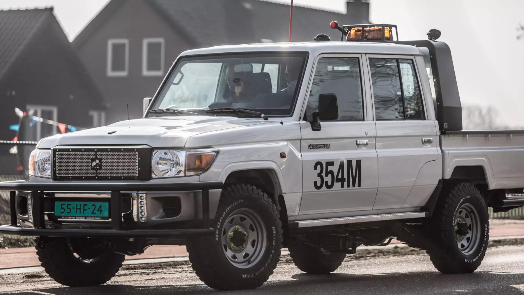 White Tembo 4x4 e-LV Land Cruiser 70 series dual-cab ute with an amber beacon, driving past houses
