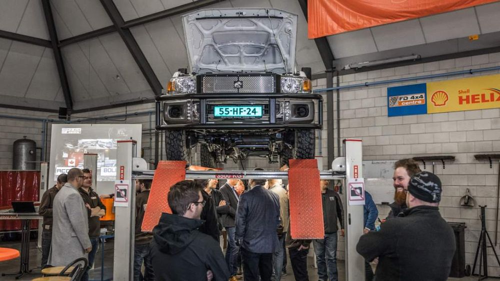 Visitors gather beneath a Tembo 4x4 e-LV Land Cruiser raised on a workshop hoist with its bonnet open
