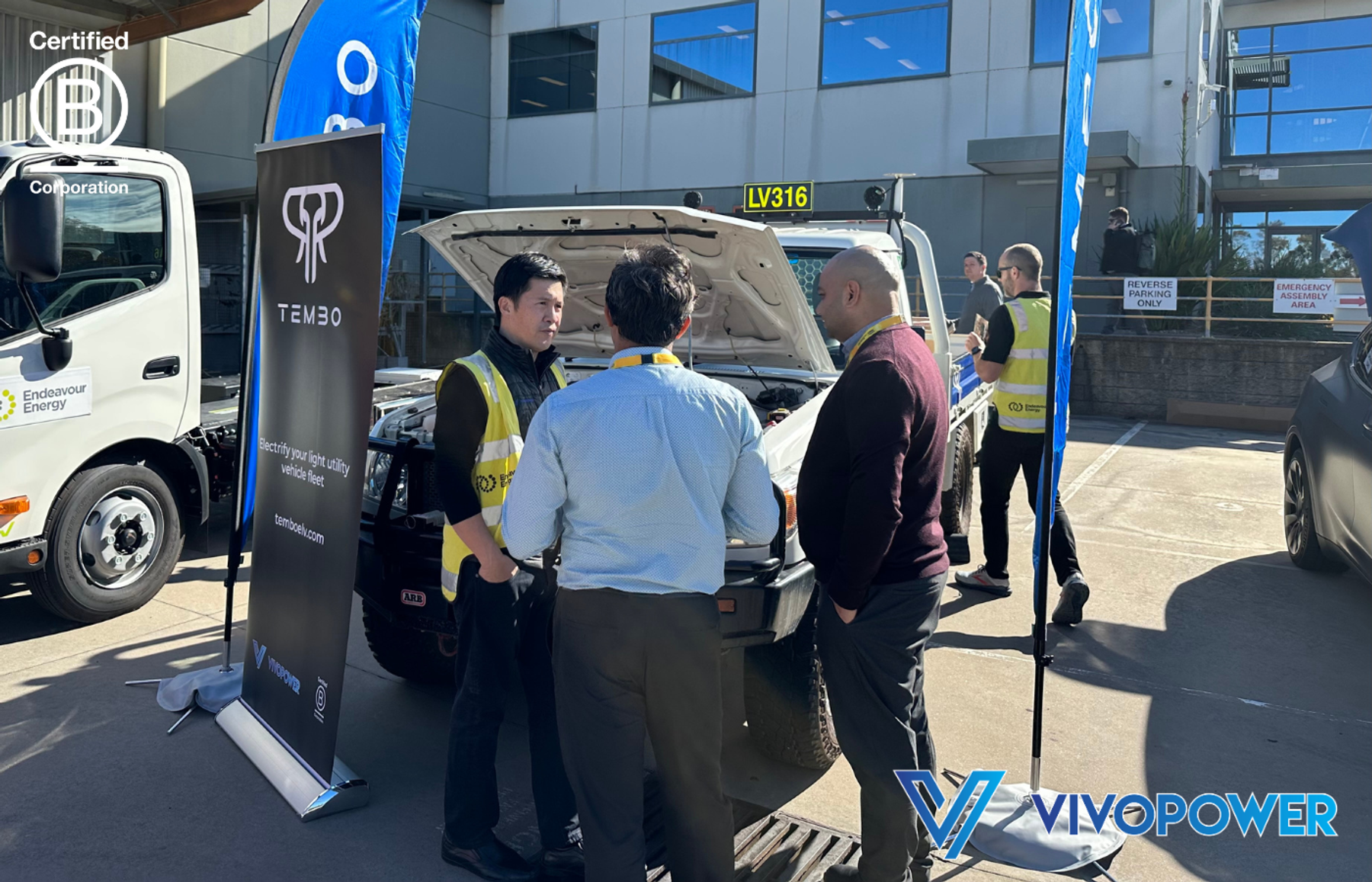 Endeavour Energy staff member talks with visitors beside a Land Cruiser ute with its bonnet open and a Tembo banner
