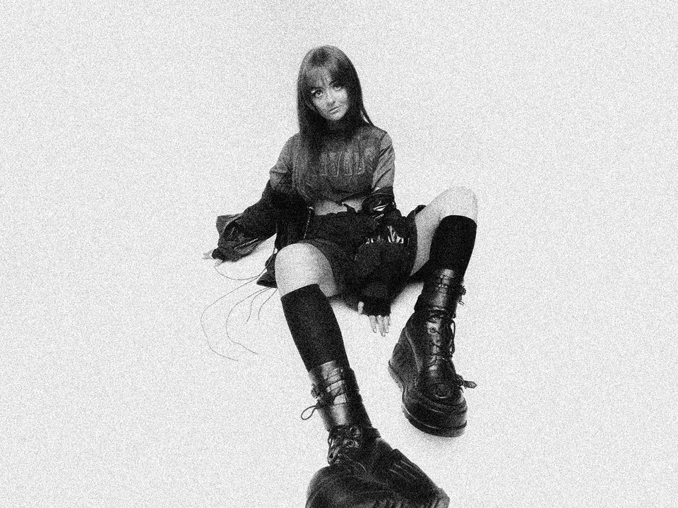 Ninajirachi poses sitting on the floor with heavy boots front and center.