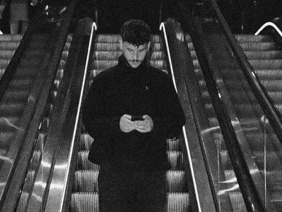 Utility goes down an escalator whilst looking down at their in-hand phone.
