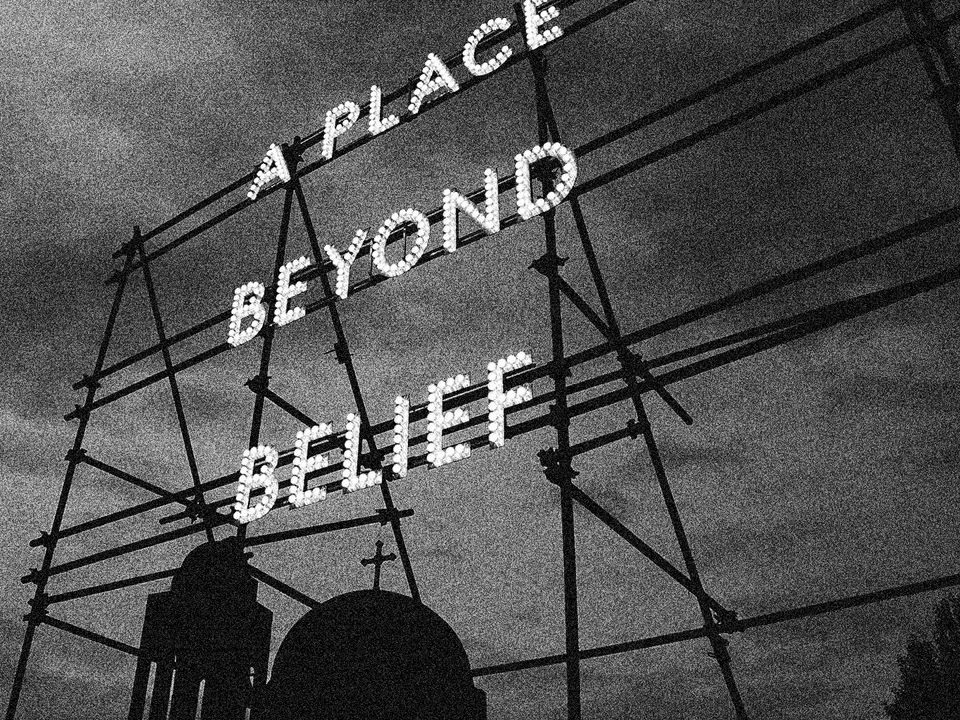 A neon sign mounted to scaffolding reads "A place beyond belief".