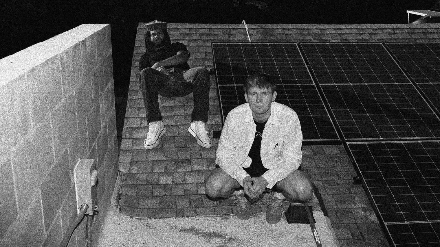 Members of Injury Reserve sit and squat on a tiled roof, beside them are several solar panels.