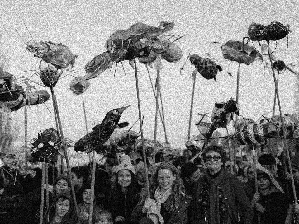 Several children hold over-sized papier-mâché insects, mounted on long poles above their heads.