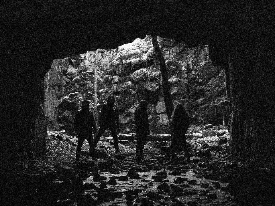 Band members of Krypts stand shrouded in darkness within a cave opening.