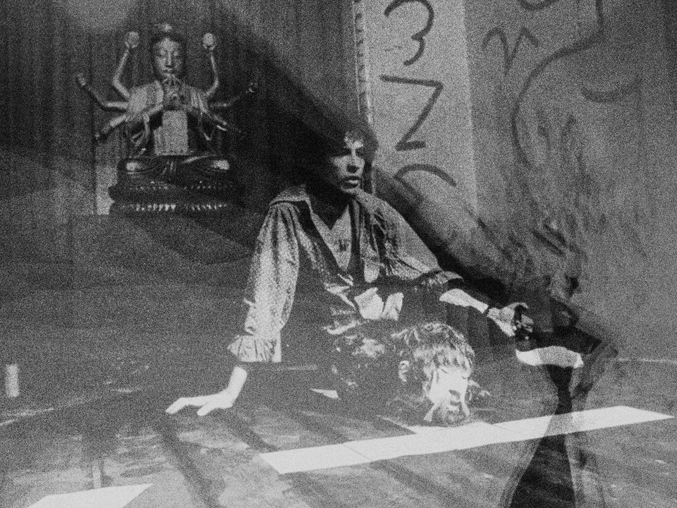 Kenneth Anger sits on the ground, on the set of Lucifer Rising. Behind him a statue of vishnu sits upon a pedestal.