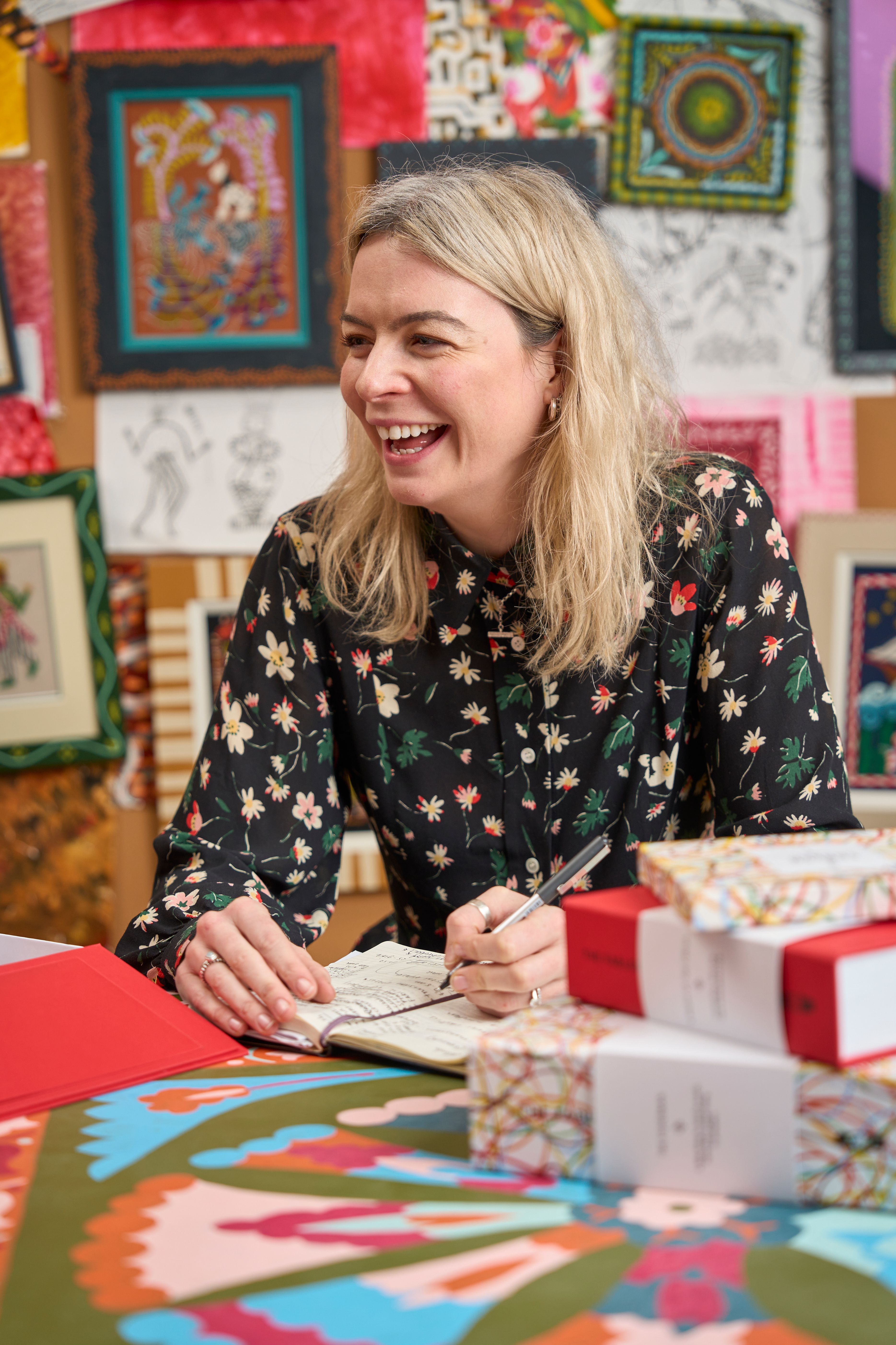 Georgina from The Fabled Thread team in the studio surrounded by embroidery kits and writing in her notebook on a painted table