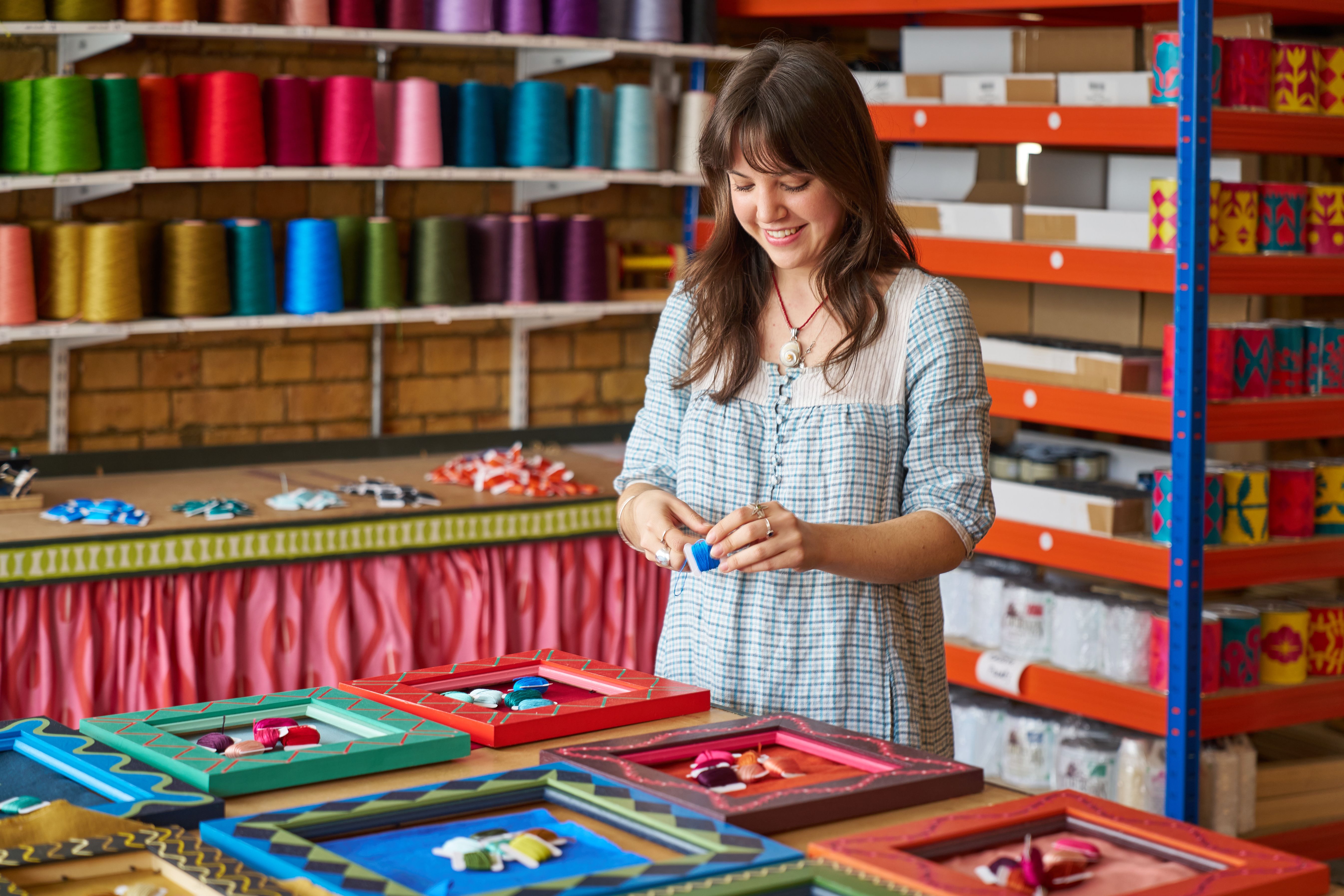 Izzy in the Studio winding embroidery bobbins in front of thread cones with painted frames on the table