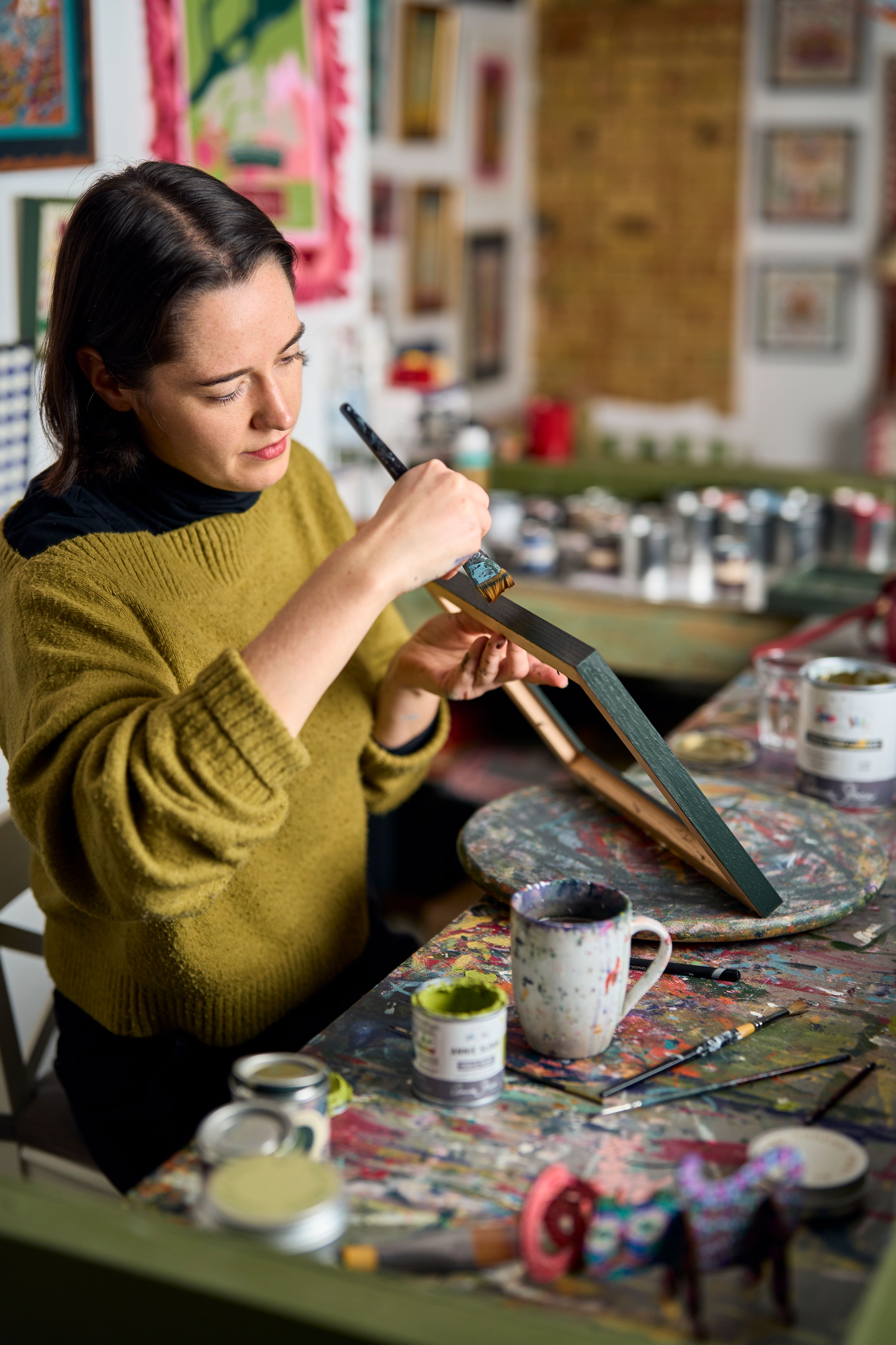 Katy in the studio at her painting station with bunting above, hand painting a frame for an embroidery kit from The Fabled Thread