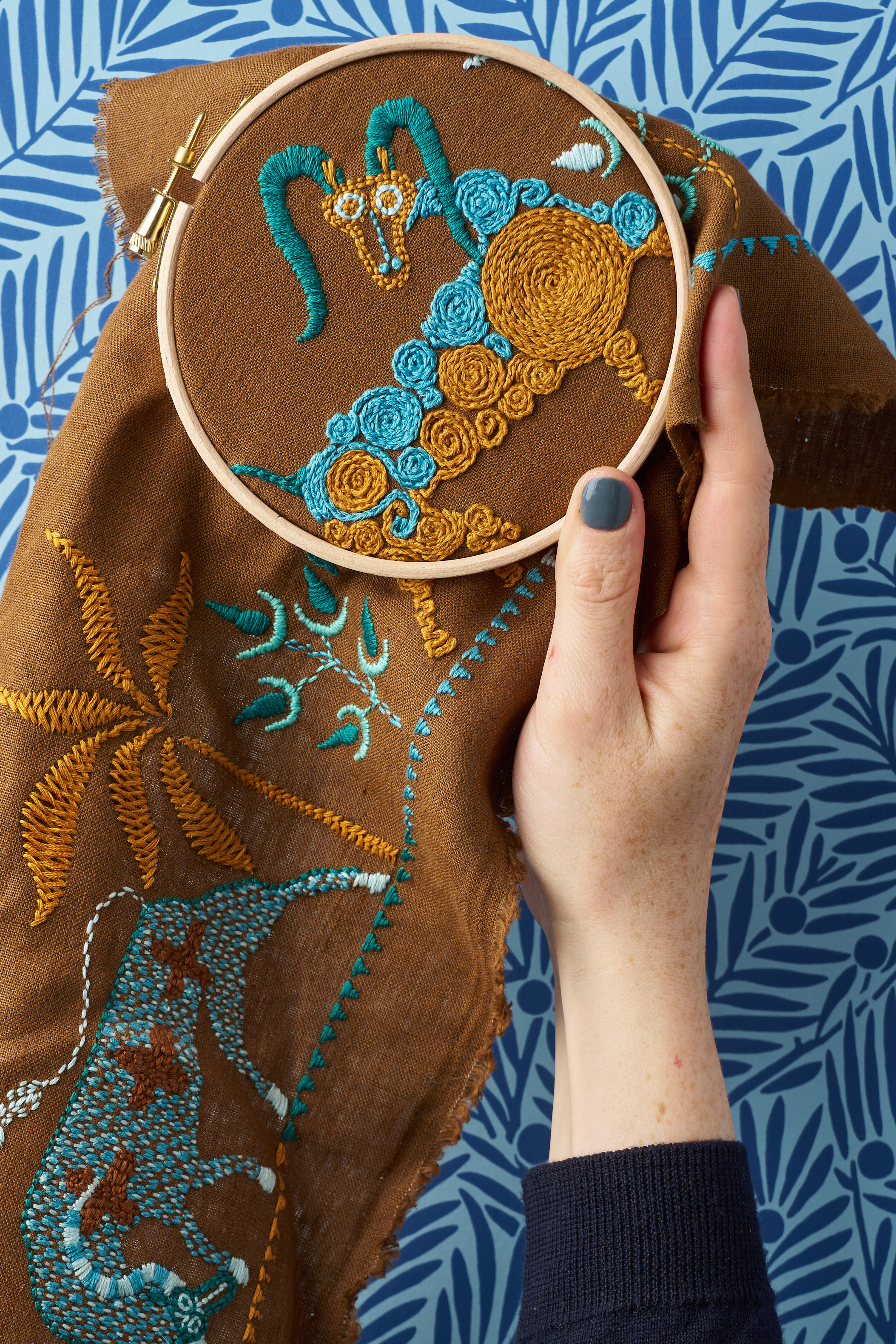 Close up of embroidery from The Fabled Thread on brown fabric in front of a blue background