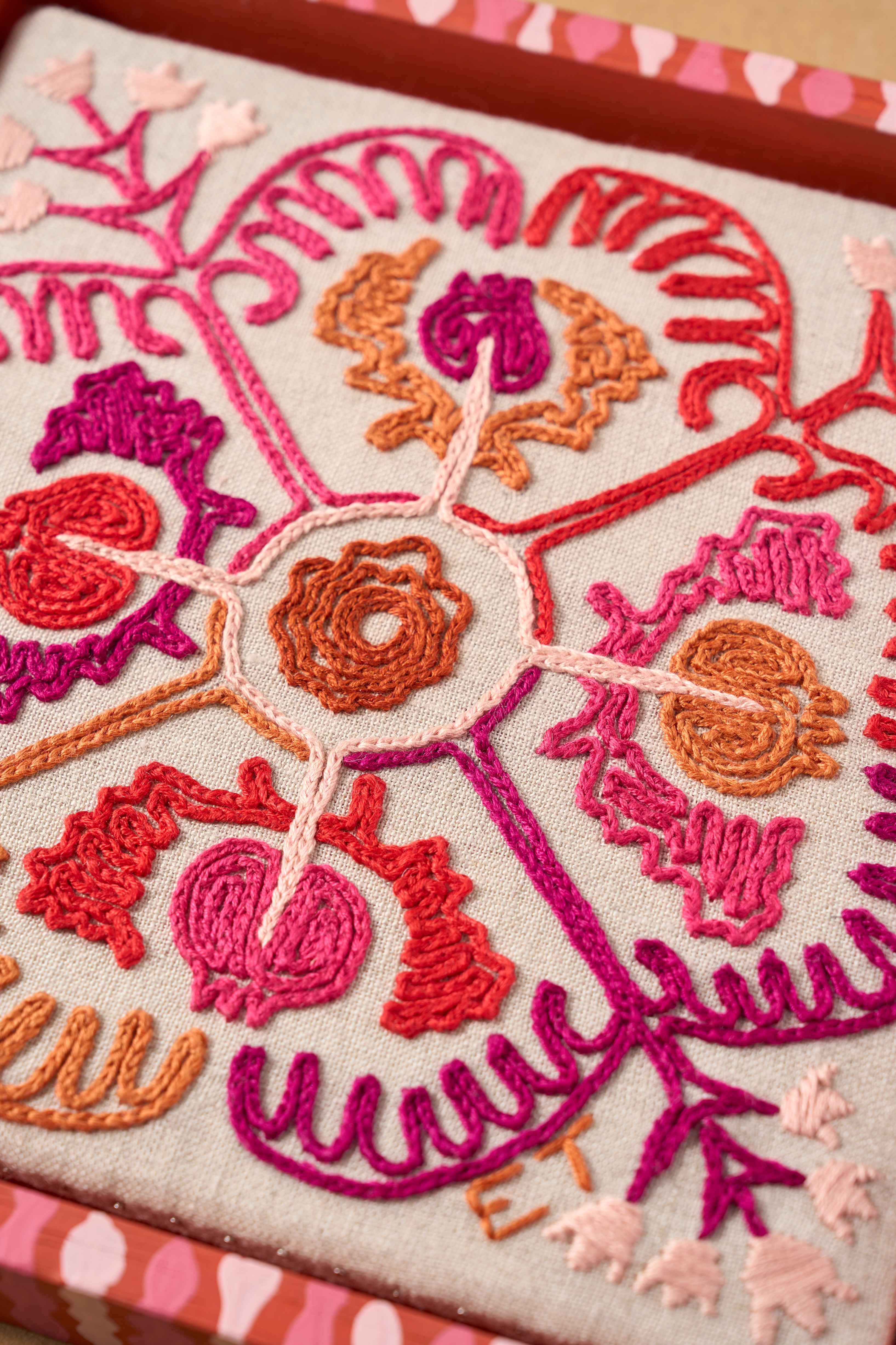 Close up of embroidery from The Fabled Thread on light fabric in a painted frame