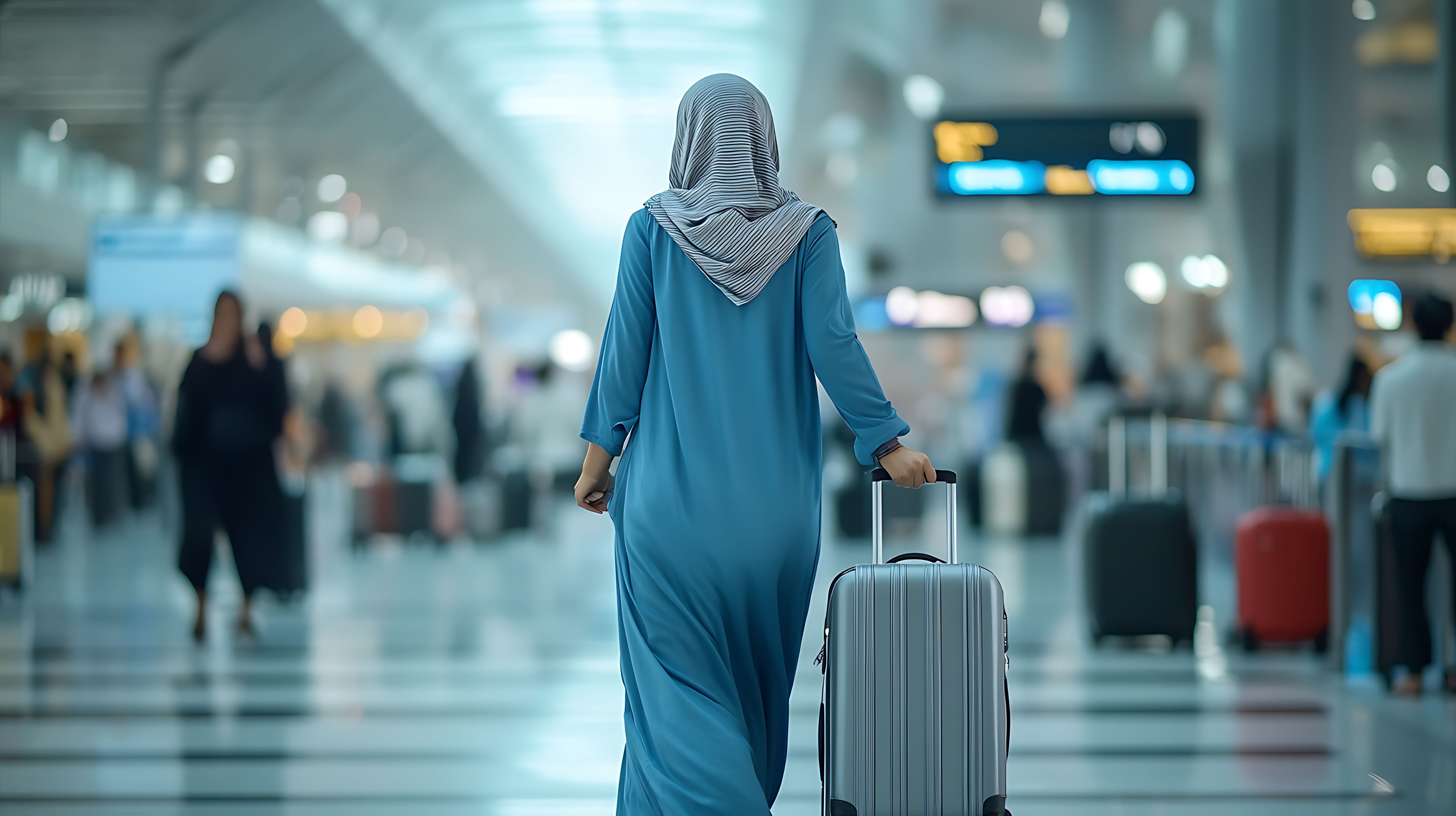 Woman in hijab pulling a suitcase through an airport terminal.