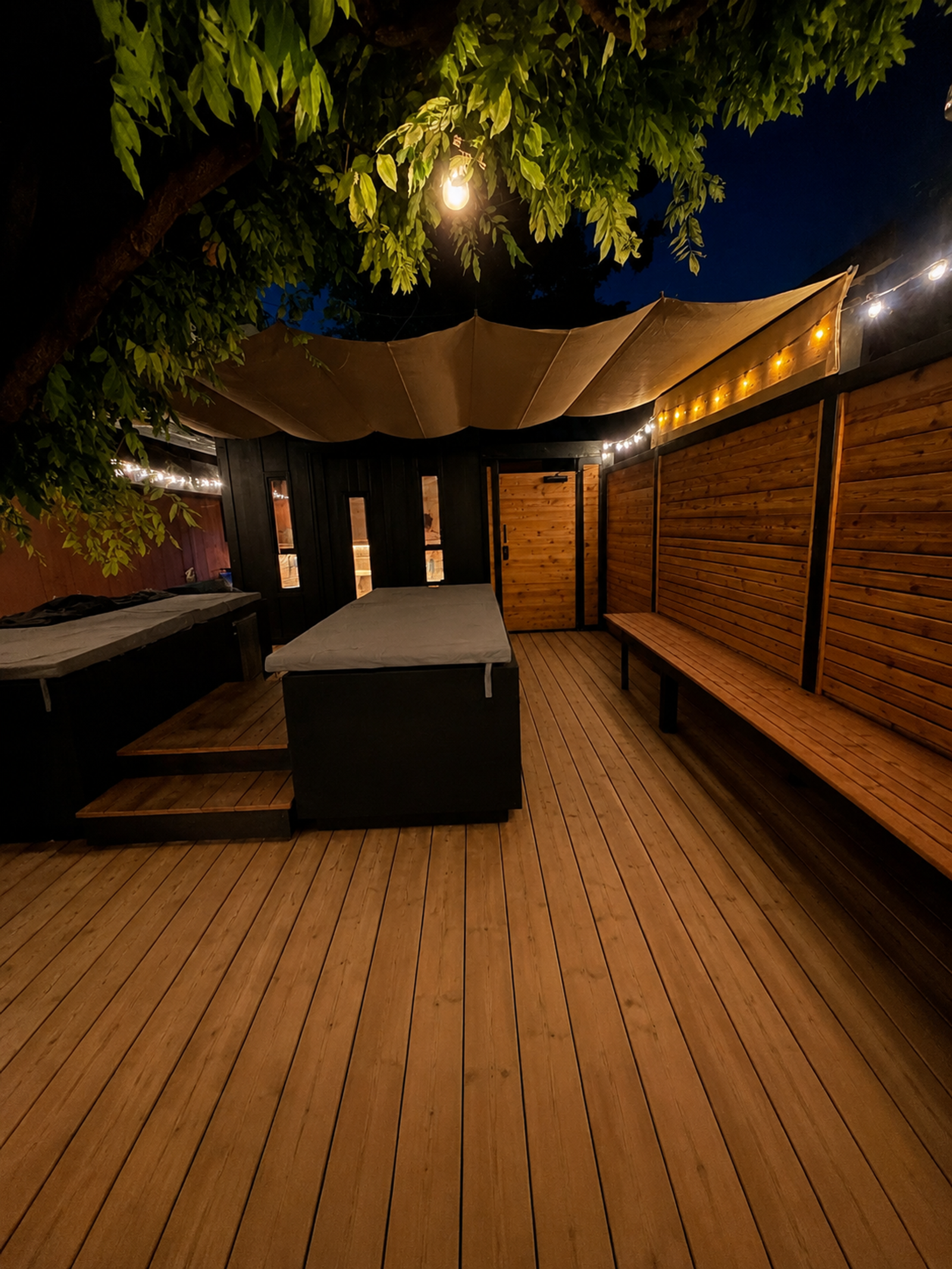 Outdoor cold plunge and sauna garden illuminated beneath shade sails and trees at Sweatcity ATX