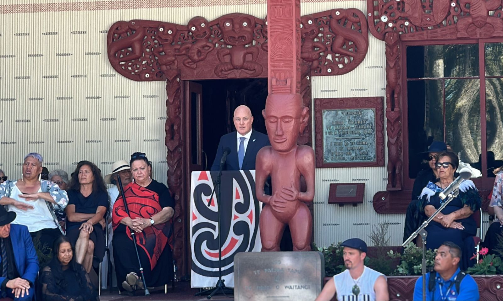 From the mahau, behind the Ngā Tamatoa flag, Luxon speaks about his party promises with scant mention of the Treaty. Photo/PMN News/Atutahi Potaka-Dewes