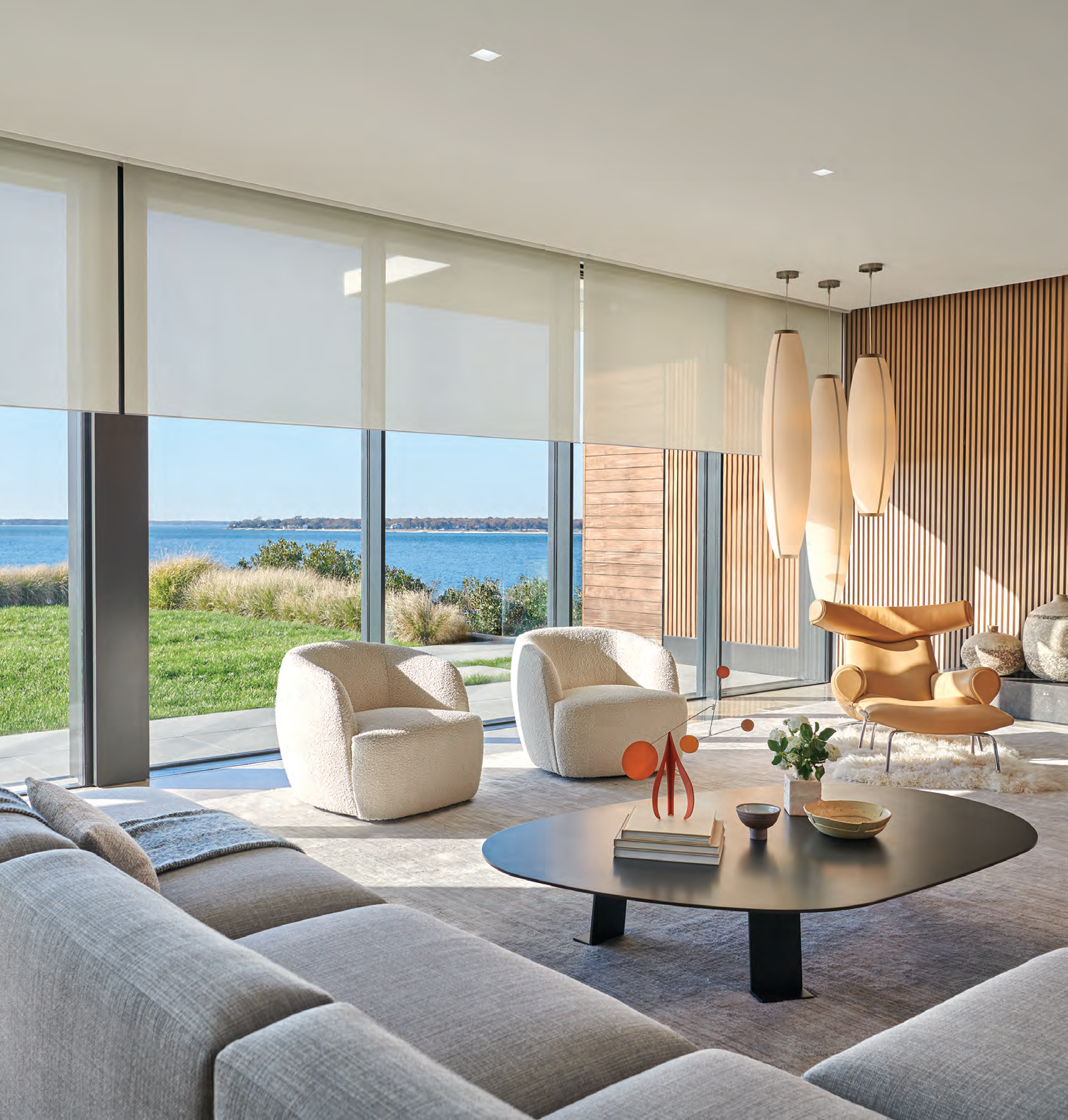 Motorized roller shades partly lowered across tall windows in a modern waterfront living room.