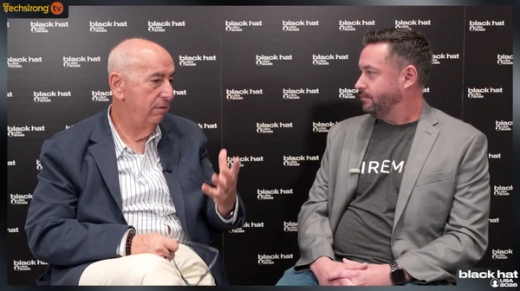 Two men in discussion at a Black Hat event, one gesturing.