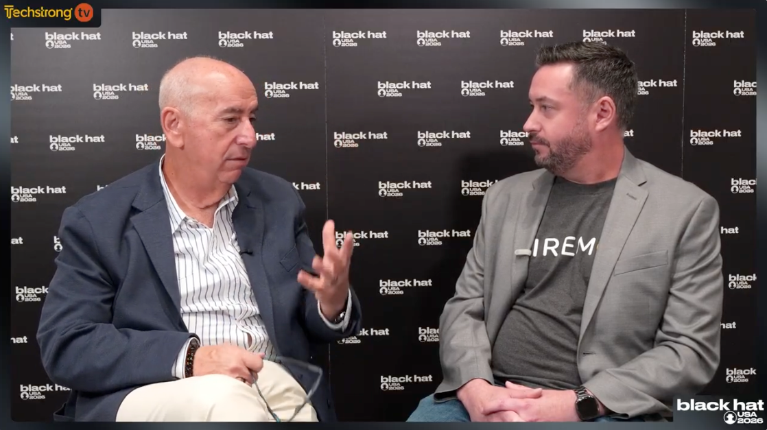 Two men in discussion at a Black Hat event, one gesturing.