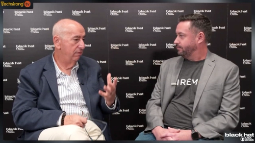 Two men in discussion at a Black Hat event, one gesturing.