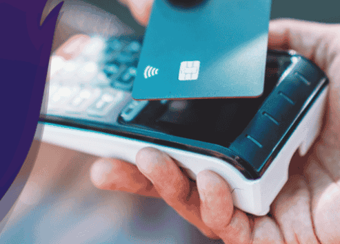 A hand uses a blue credit card for a contactless payment on a terminal.