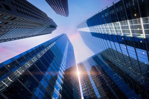 Low-angle view of modern skyscrapers with blue glass facades and a sun flare.