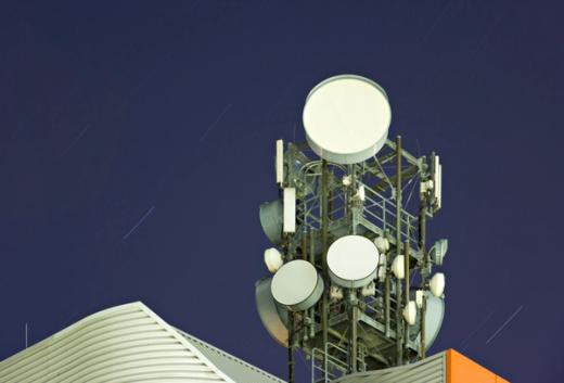 A communication tower with multiple dishes and antennas against a dark night sky with faint star trails.