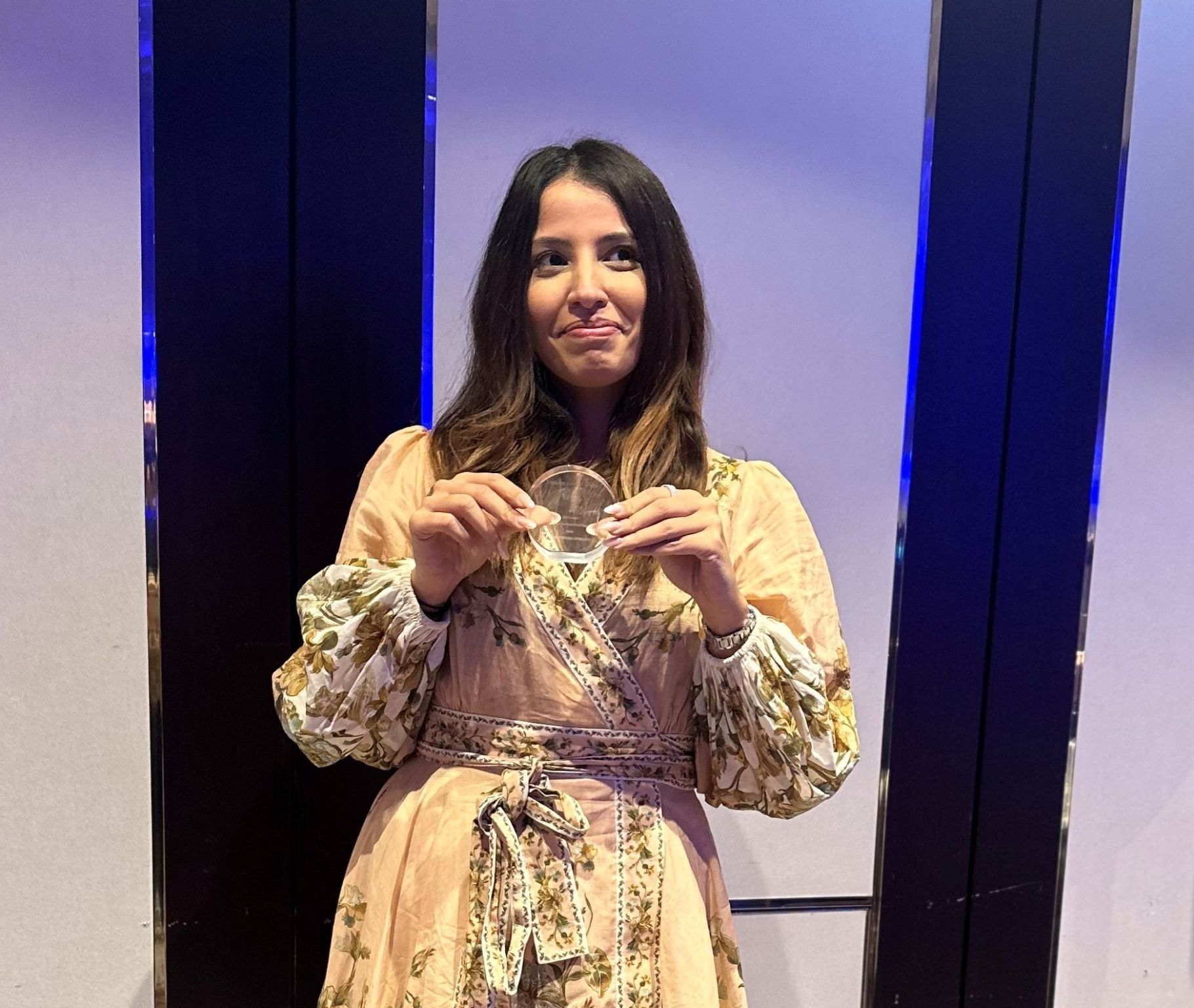 Femme souriante en robe fleurie tenant un trophée circulaire lors des Private Equity Africa Awards