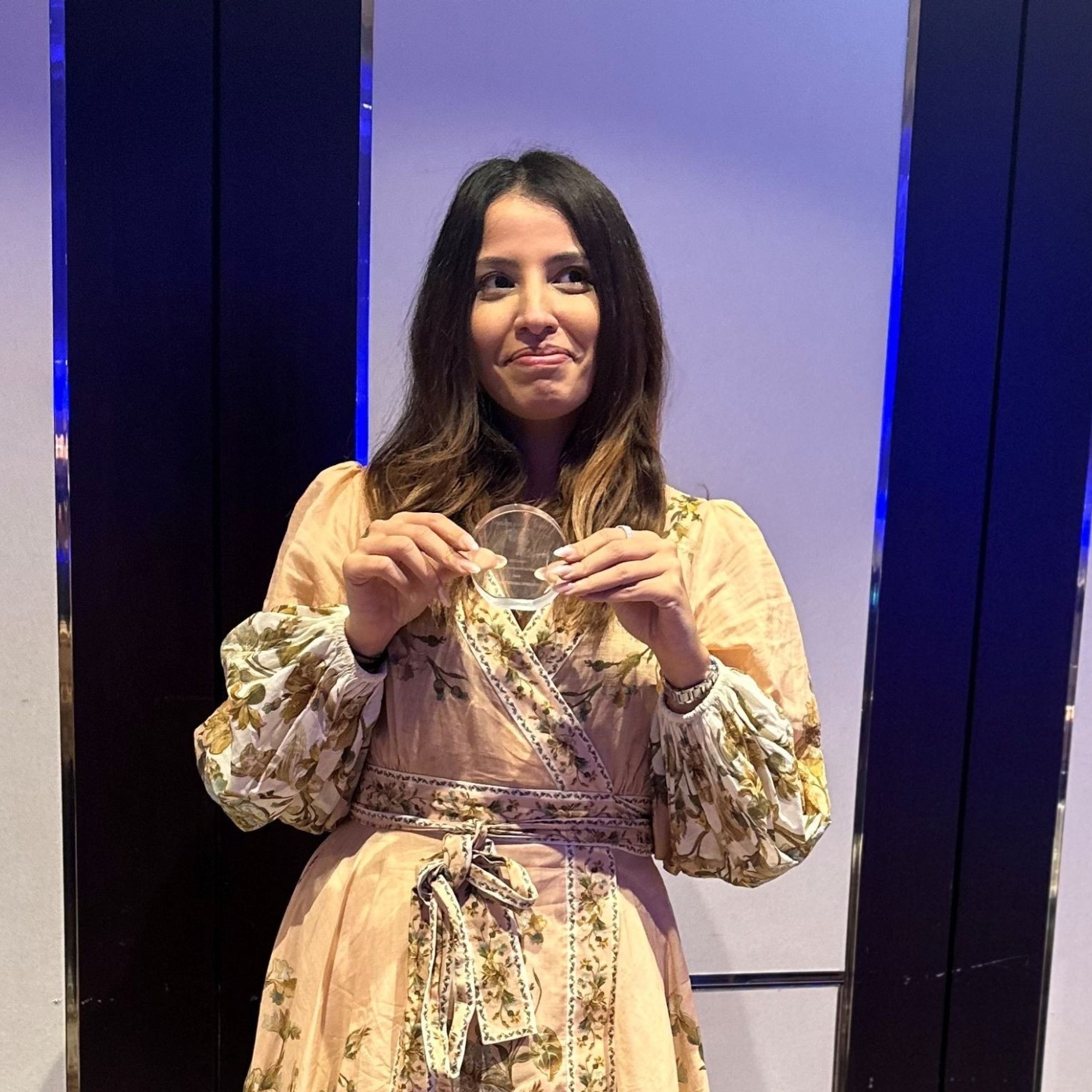 Femme souriante en robe fleurie tenant un trophée circulaire lors des Private Equity Africa Awards