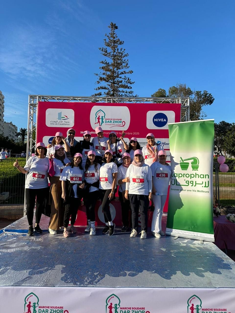 Groupe de femmes en t-shirts blancs et casquettes roses posant sur un podium lors de la marche solidaire Dar Zhor