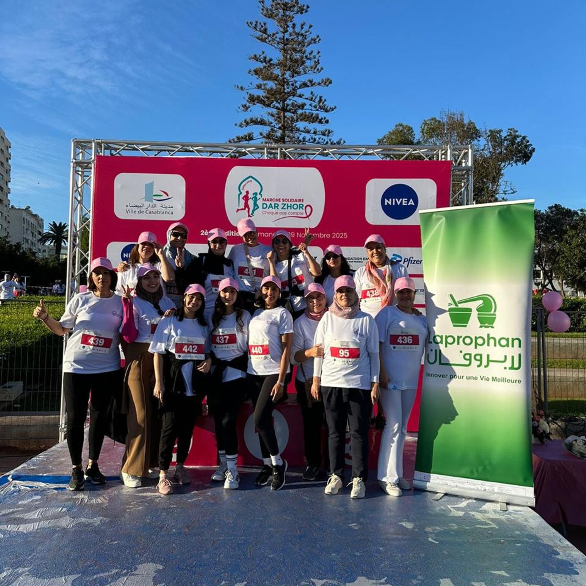 Groupe de femmes en t-shirts blancs et casquettes roses posant sur un podium lors de la marche solidaire Dar Zhor