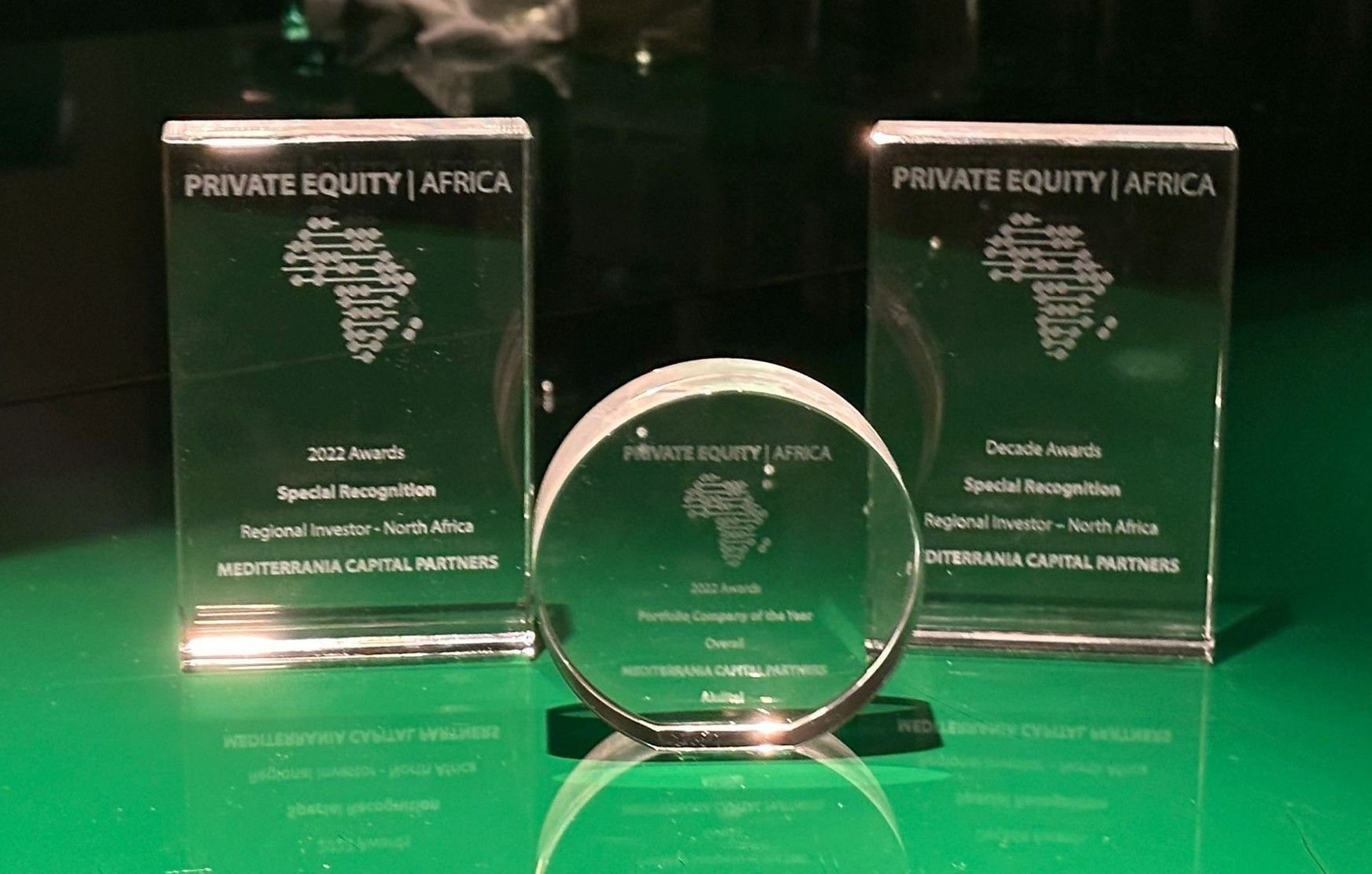 Trois trophées en verre Private Equity Africa décernés à Mediterrania Capital Partners sur un support vert brillant