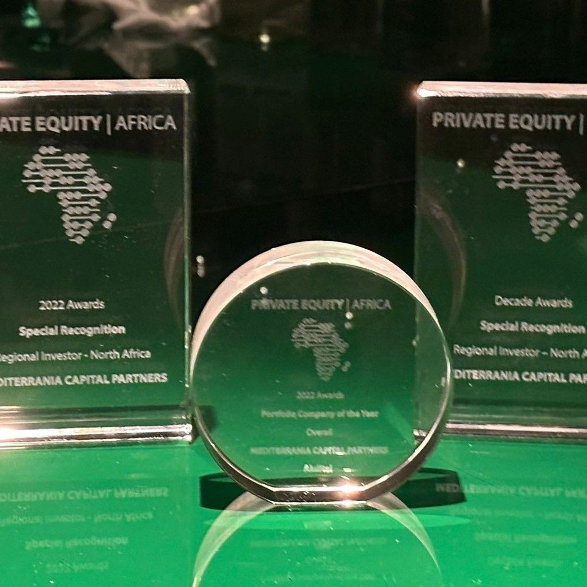 Trois trophées en verre Private Equity Africa décernés à Mediterrania Capital Partners sur un support vert brillant