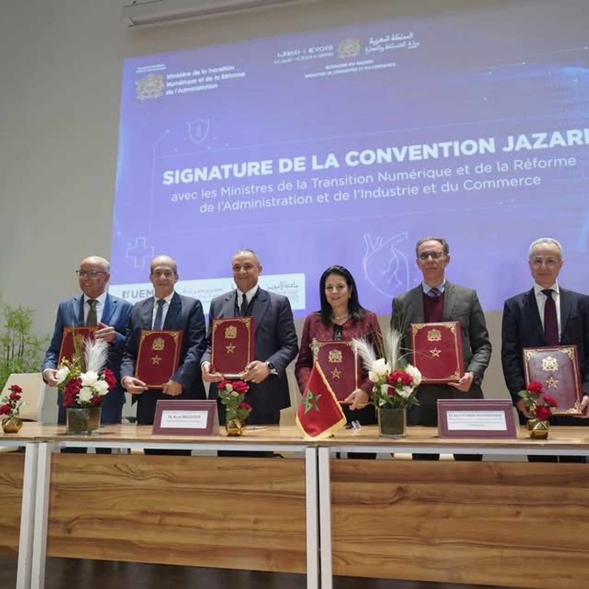 Signature de la convention Jazari par six officiels tenant des dossiers rouges devant un écran de conférence à l'UEMF