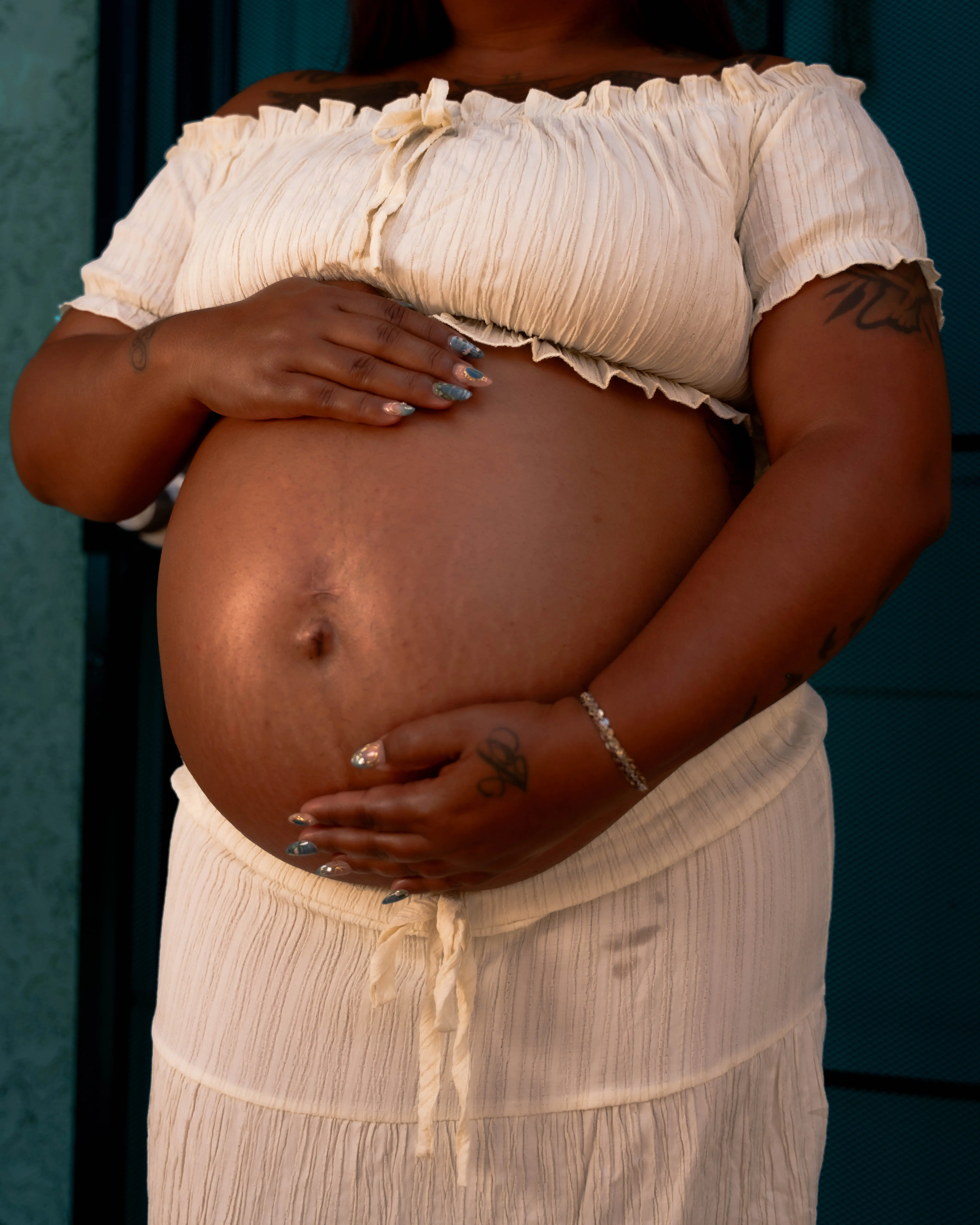 An expectant mother from Watts gently cradles her belly between her arms