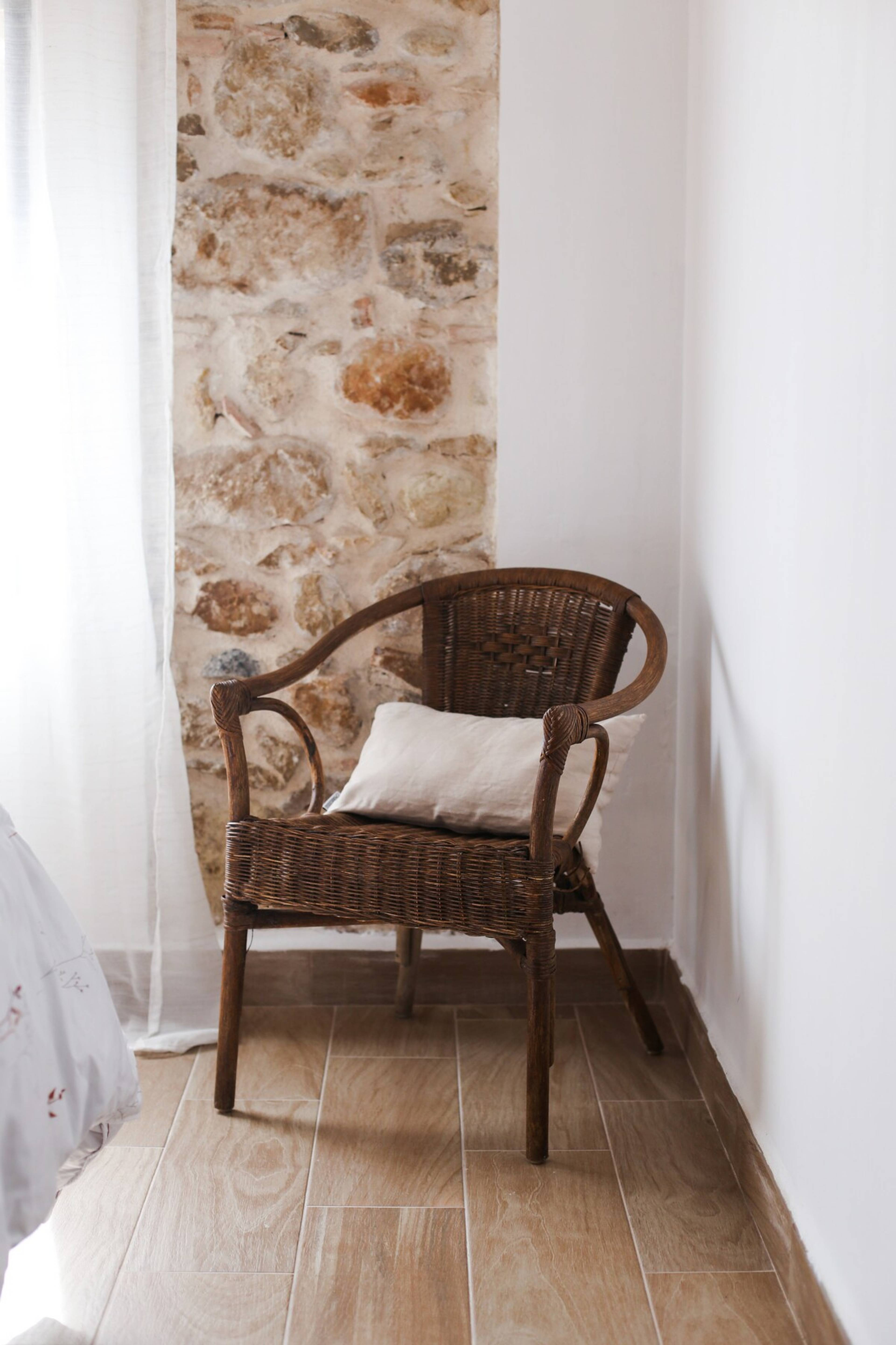 Sillón de mimbre junto a la ventana y pared de piedra natural