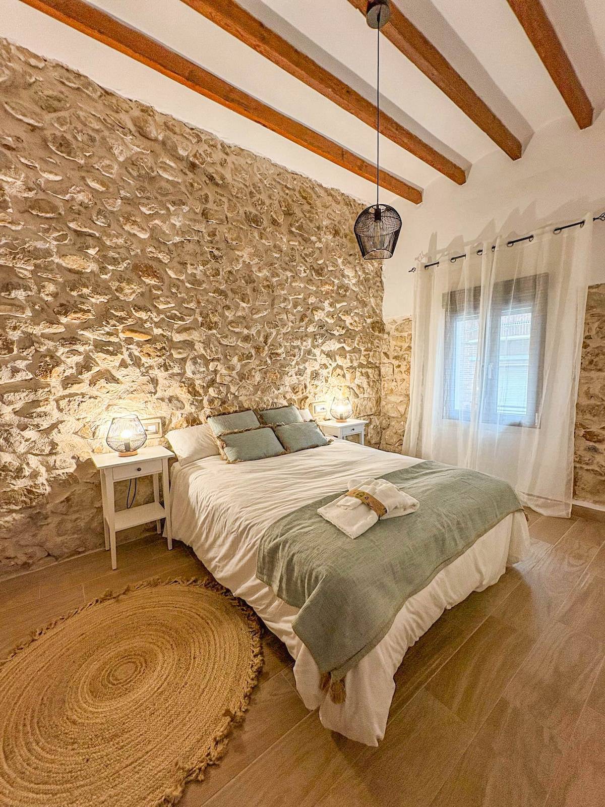 Dormitorio con cama de matrimonio, pared de piedra y ventana
