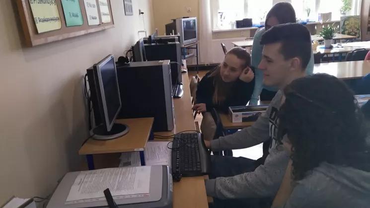 Uczniowe szkoły siędzący przy komputerze w szkolnej bibliotece