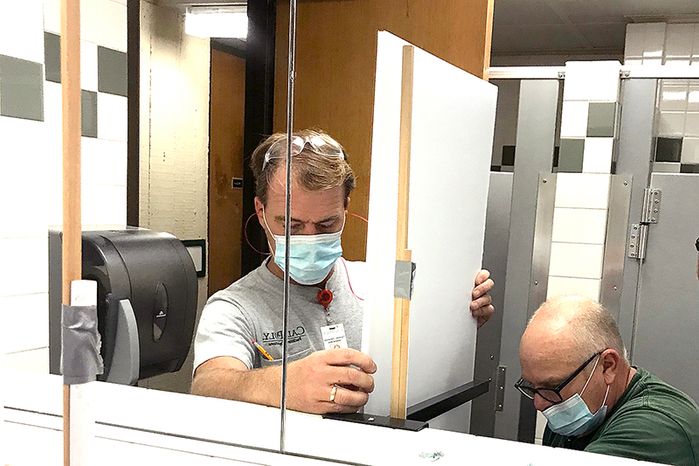 Facilities Operations team members install a partition in a restroom